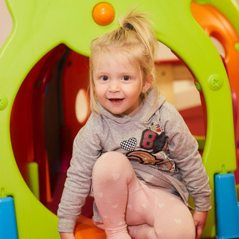 Toddler girl playing inside colorful caterpillar play tunnel at daycare